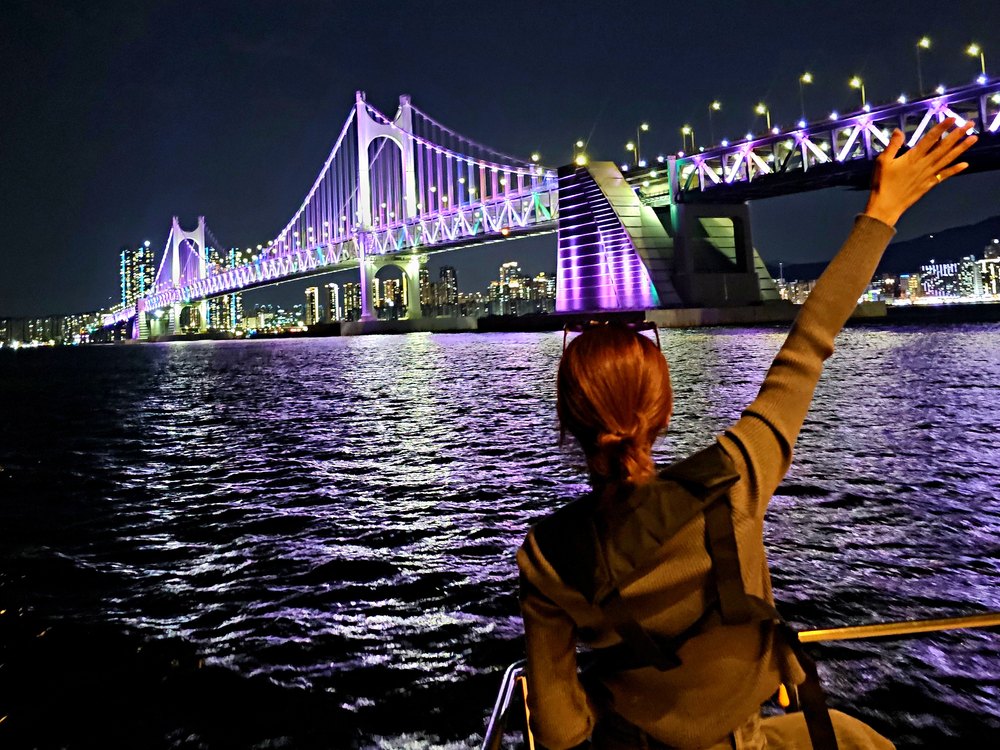Guest on a yacht reaching toward the Gwangan Bridge night view